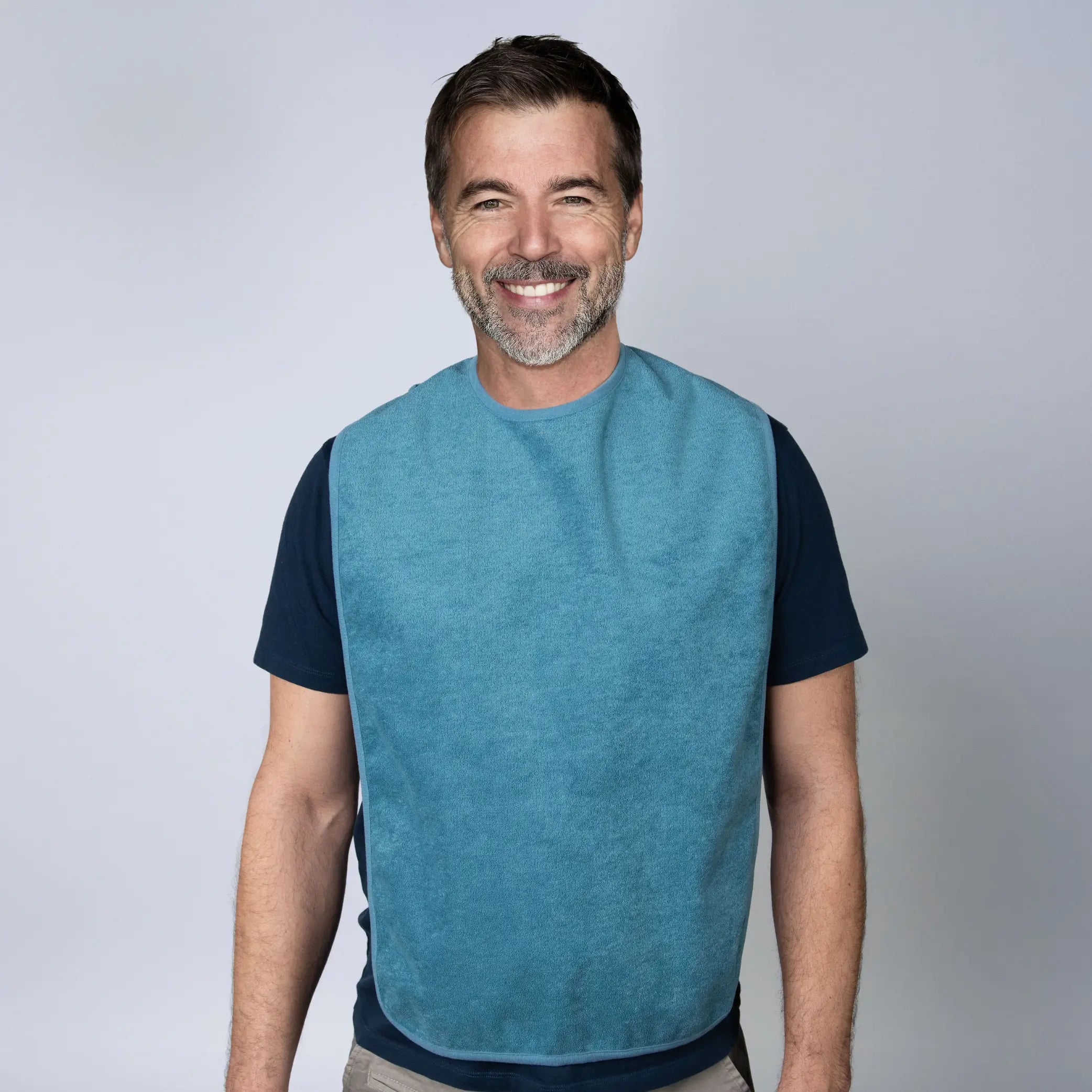 StayDry absorbent and waterproof clothing protector in teal, worn by a smiling man. Designed for adults and seniors, this stylish bib provides full-coverage protection from spills, stains, and moisture, featuring a soft, absorbent fabric with an easy hook-and-loop closure.