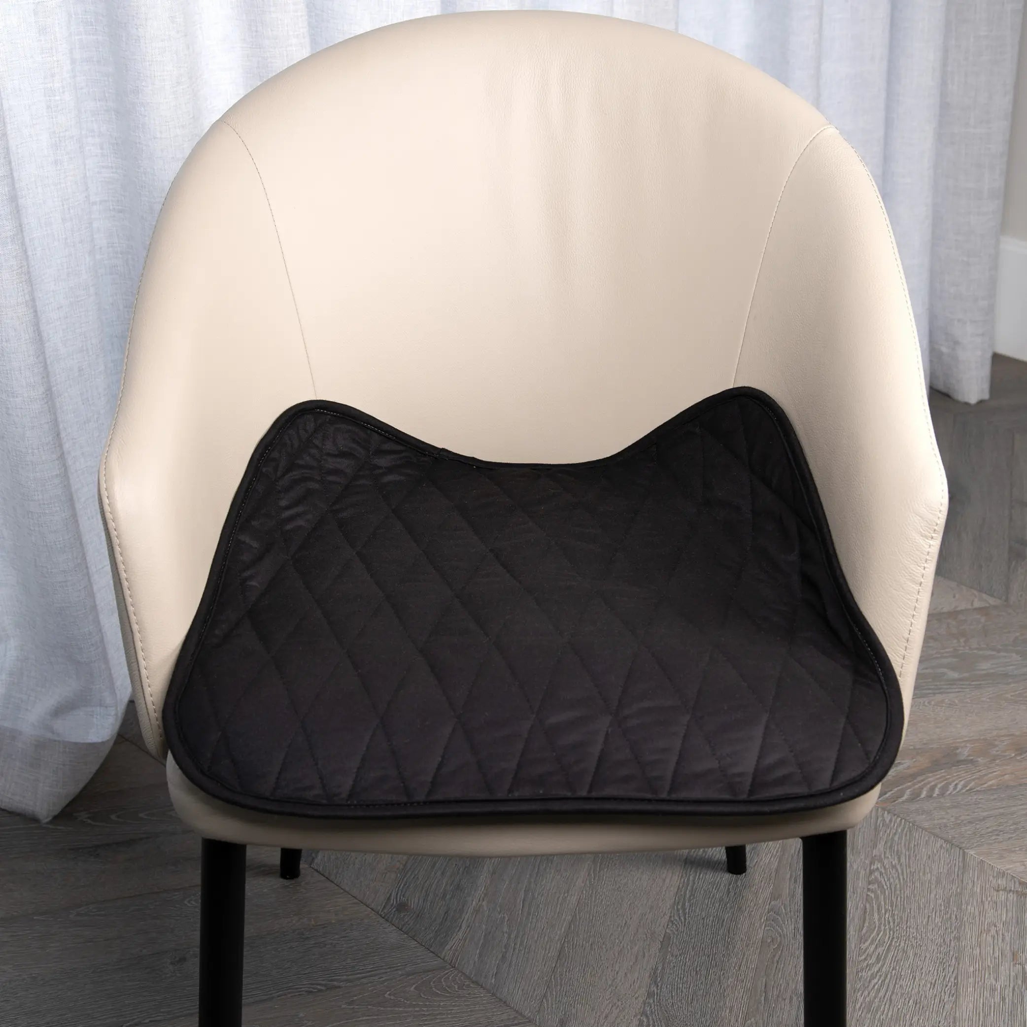 Black waterproof chair pad with a quilted design placed on a beige upholstered chair, offering protection from spills, leaks. Perfect for dining chairs, office chairs, wheelchairs, and incontinence support.