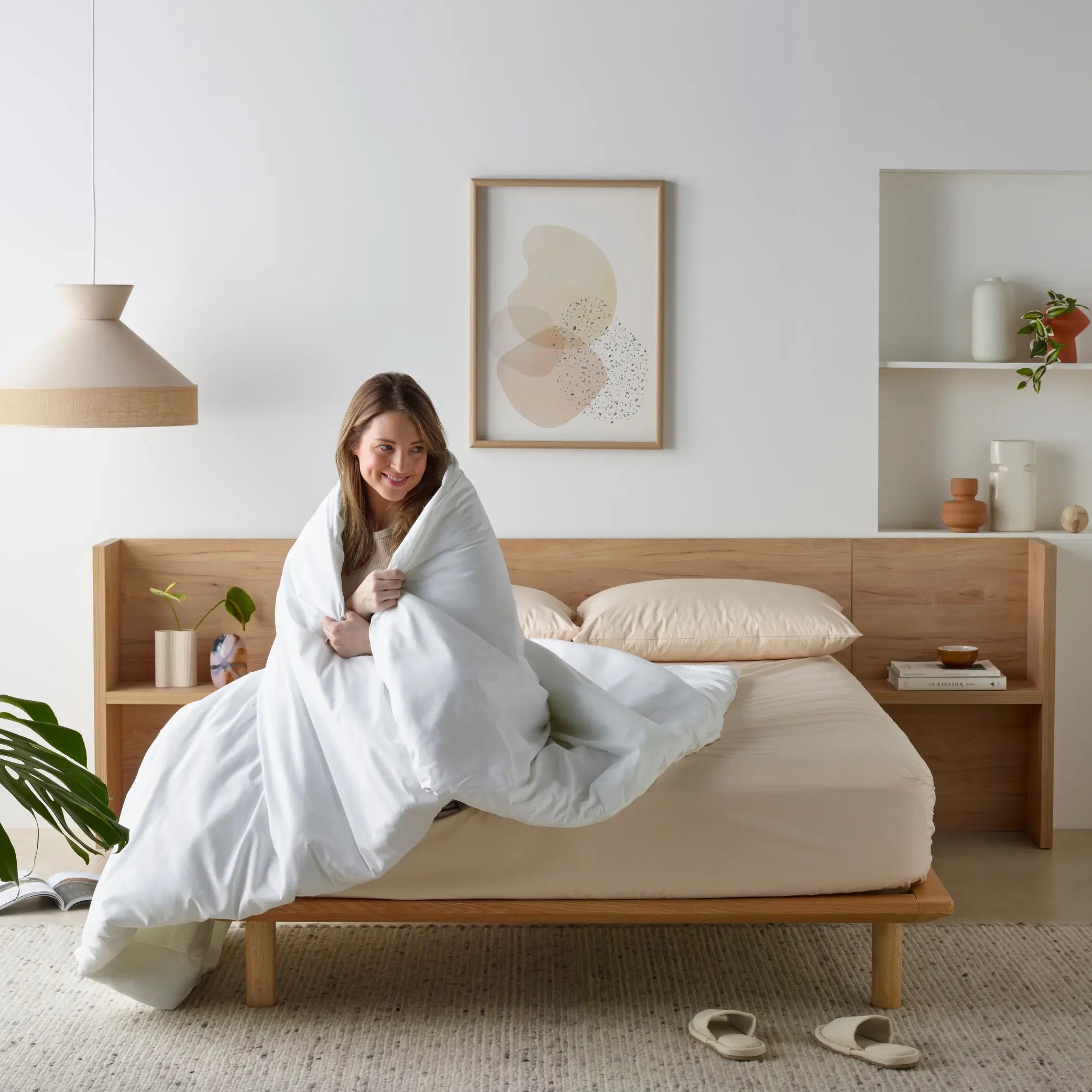 Woman wrapped in the Everyday Easy Water-Resistant Quilt, enjoying warmth and comfort in a modern, minimalist bedroom. This waterproof quilt offers protection against spills and moisture, making it a durable and cosy choice for everyday use.