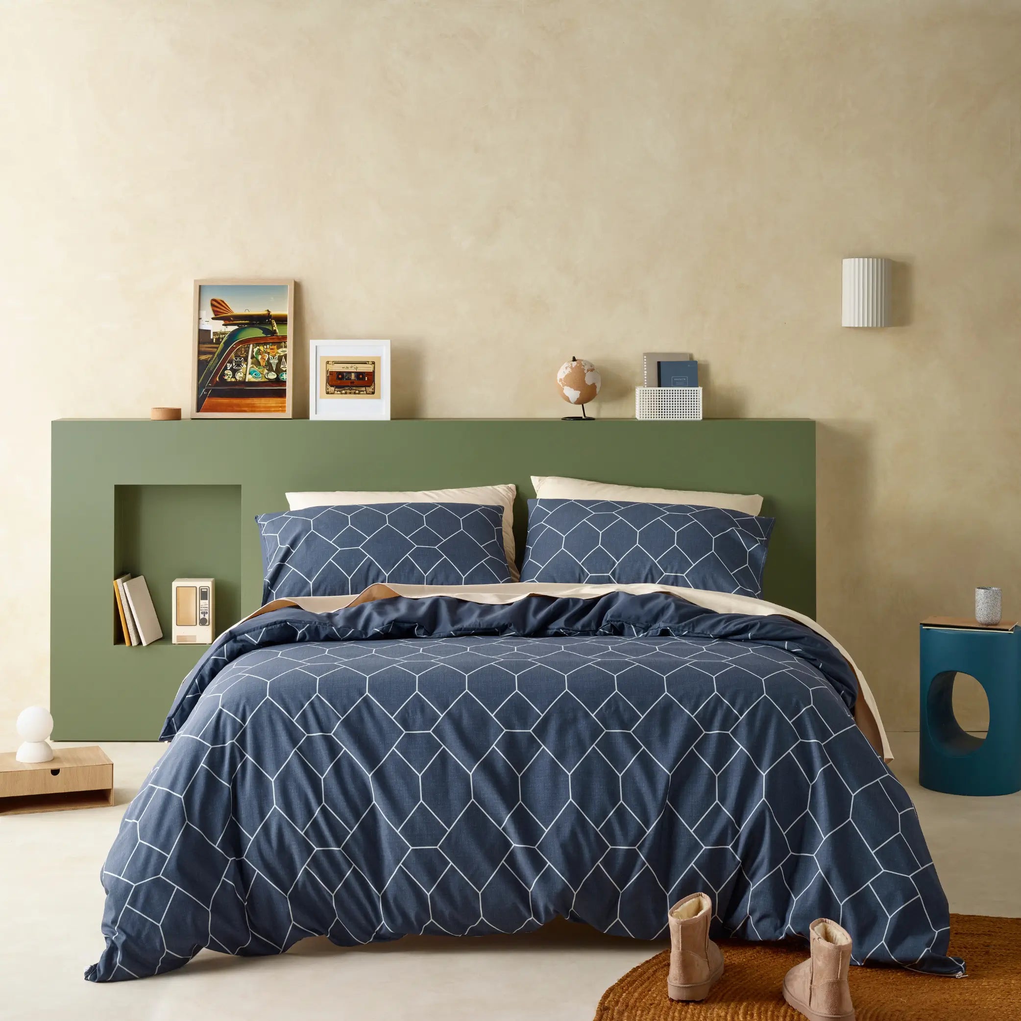 Modern bedroom featuring a navy blue geometric quilt cover set with a crisp white hexagonal pattern. The bedding design adds a contemporary touch, complemented by neutral decor, a soft olive-green bedhead, and minimalist styling for a cosy yet stylish aesthetic.