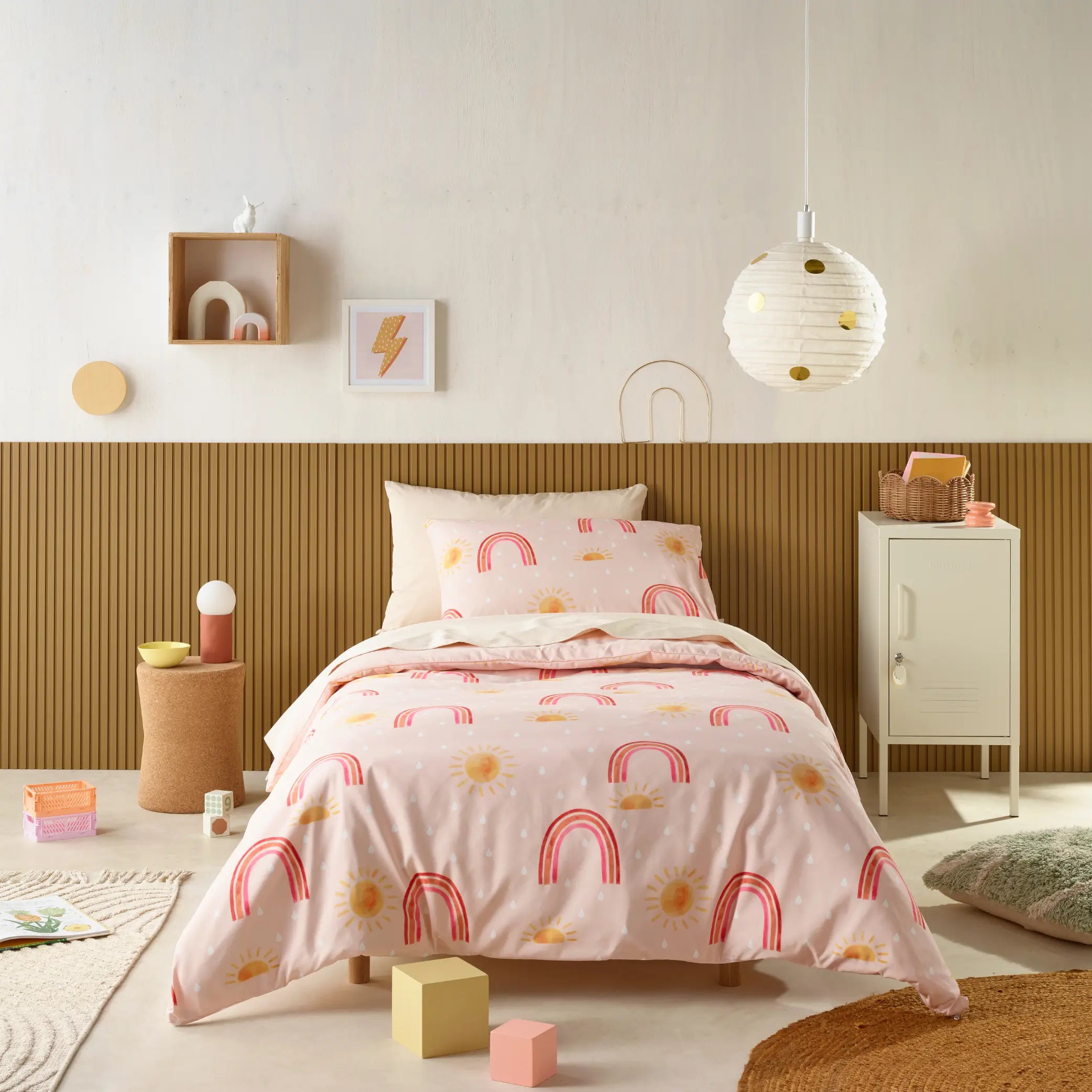 Kids' bedroom styled with a water-resistant quilt cover set featuring a playful pink design with rainbows, suns, and soft white dots.