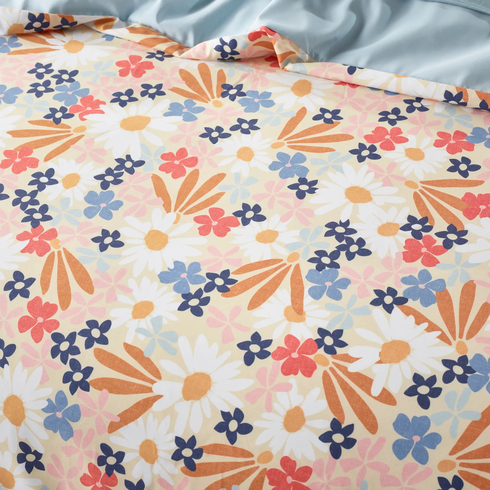 Close-up of a vibrant floral quilt cover featuring a playful daisy pattern in warm and cool tones. The detailed print showcases a mix of white daisies, blue, coral, and orange flowers on a soft pastel background.