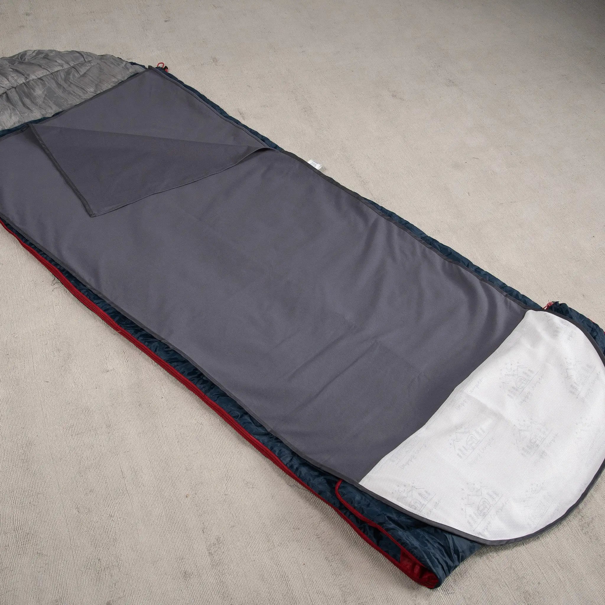 Grey waterproof and absorbent sleeping bag liner laid out on a beige carpet, featuring a soft fabric top layer and a waterproof backing for protection. Ideal for camping, travel and incontinence support.