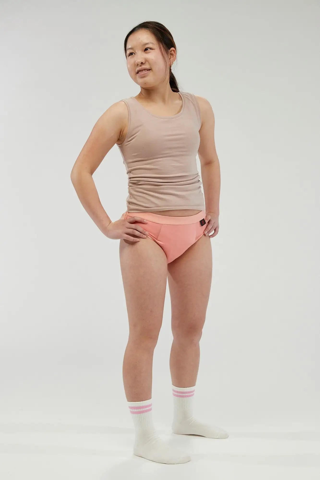 Teen girl wearing peach pink incontinence underwear with a comfortable, discreet fit. Designed with a built-in absorbent core, leak-proof protection, and breathable, moisture-wicking fabric for all-day confidence. These machine-washable, reusable briefs provide a secure and stylish alternative to traditional incontinence products, ideal for active lifestyles.