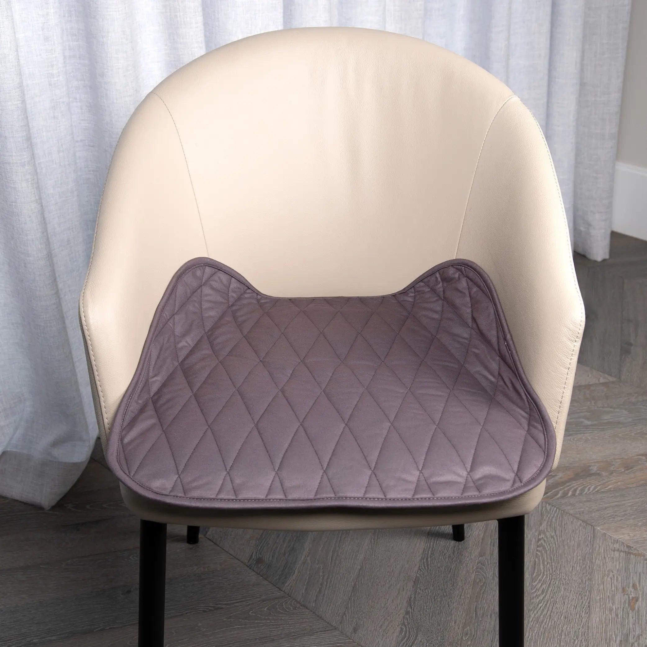 Grey waterproof chair pad with a quilted design placed on a beige upholstered chair, providing a comfortable and protective layer against spills, leaks, and daily wear. Perfect for dining chairs, office chairs, wheelchairs, and incontinence support.