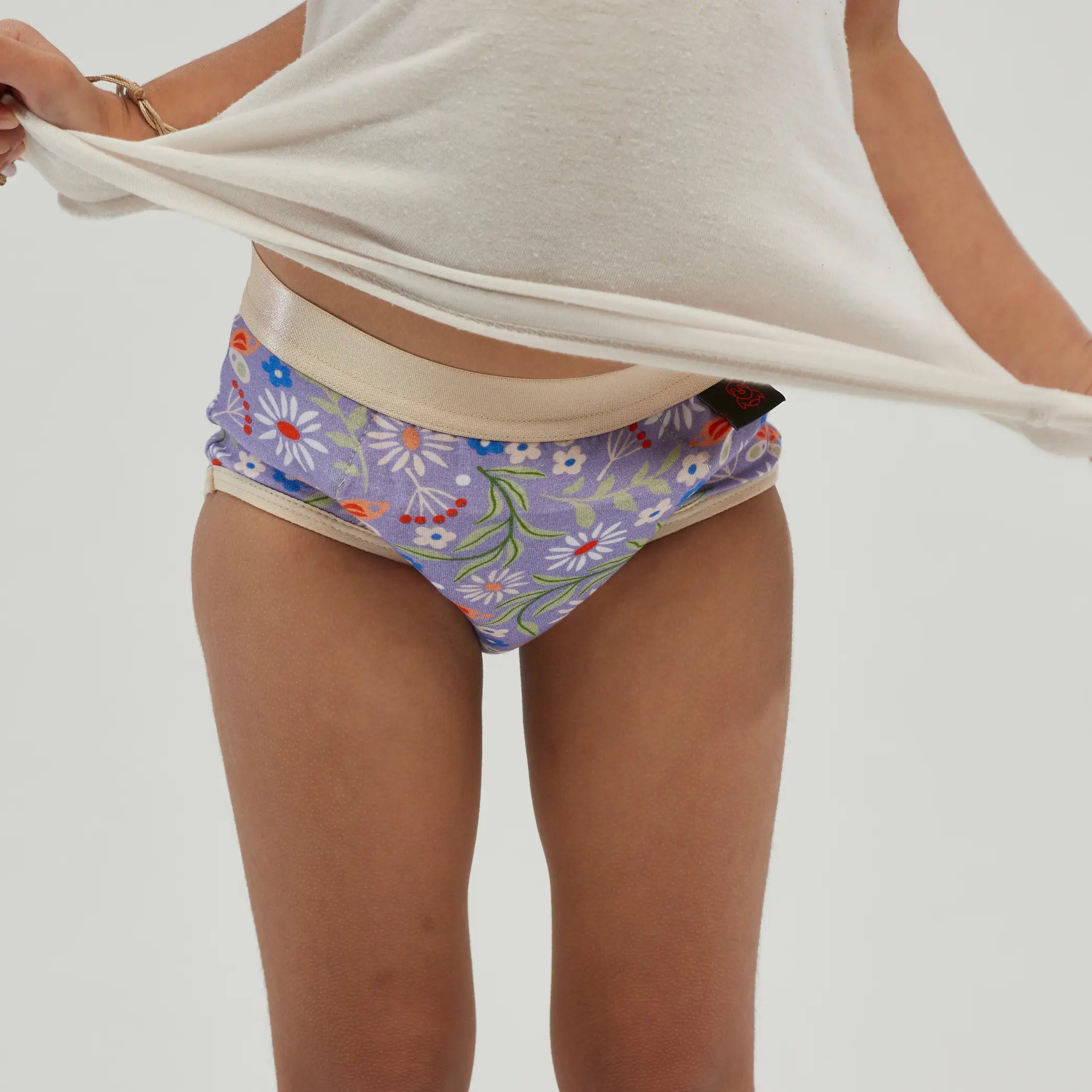 Front view of children's incontinence underwear with a soft lilac floral pattern and a beige waistband. These reusable undies feature an absorbent, leak-proof core designed for overnight and daytime protection. Made from breathable, moisture-wicking fabric, they offer comfort and security for kids managing incontinence. The stretch-fit waistband and snug leg openings provide a secure fit without discomfort.