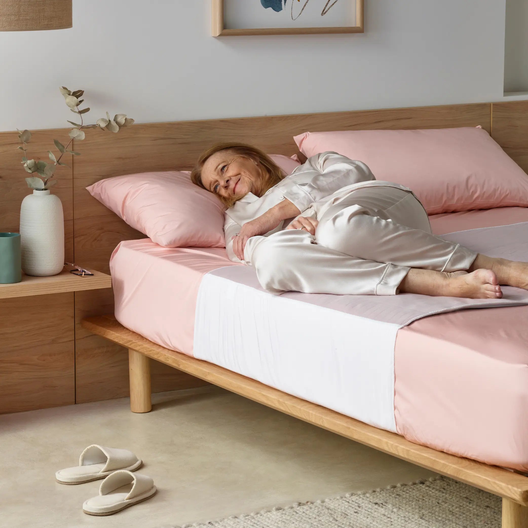 Elderly woman comfortably resting on a bed with a soft pink waterproof bed pad. Designed for incontinence protection, this breathable and washable bed pad keeps bedding dry and ensures a restful sleep.